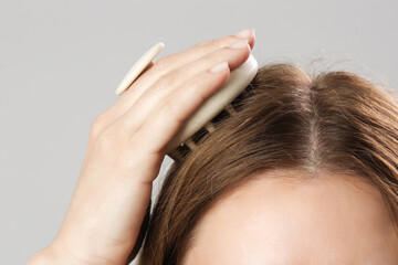 Fototapeta premium Girl doing herself a head massage using a scalp massager, stimulating hair growth, microcirculation, help to distribute natural oils more evenly across the scalp