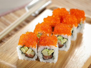 A plate of sushi with avocado and salmon on top of a wooden board