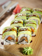 A plate of sushi with a green avocado roll and a red garnish