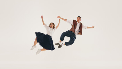 Retro lindy hop dancers perform a mid-air jump against a plain white background. Concept of vintage dance styles and joyful expression.