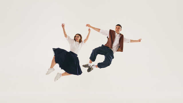 Retro lindy hop dancers perform a mid-air jump against a plain white background. Concept of vintage dance styles and joyful expression.