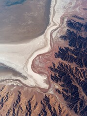 Low-altitude aerial view of Desert's white lake with pink salt, mountains, rivers and ripples.
