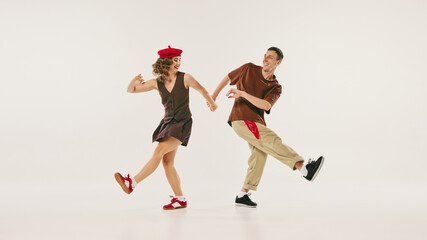 A retro duo performs an energetic lindy hop dance move in vintage-inspired outfits on a white background. Concept of nostalgic dance performance and cultural preservation.