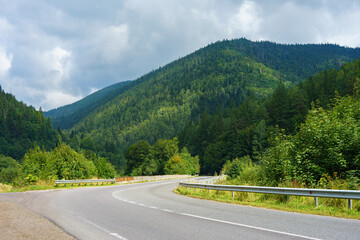 Scenic winding road through lush green forested hills in the Ukrainian Carpathians under dramatic cloudy sky. Perfect landscape for travel, tourism, and nature themes.