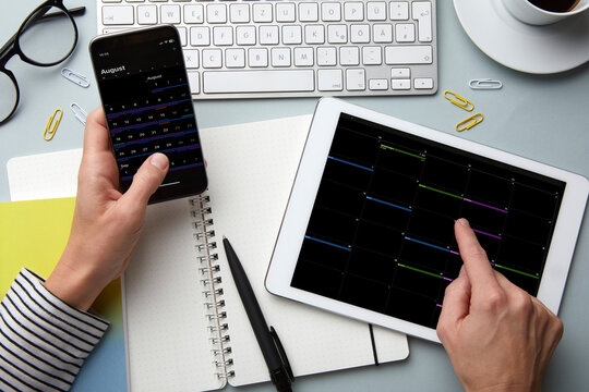 Person using smartphone and tablet for calendar planning at a desk