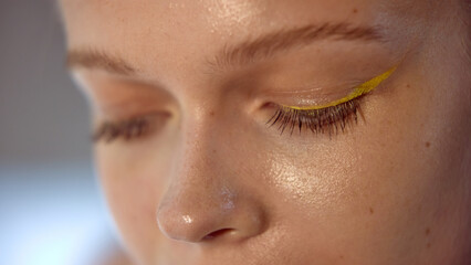 Dopamine makeup. Closeup of an eye featuring bold yellow eyeliner and a natural makeup look on fair...