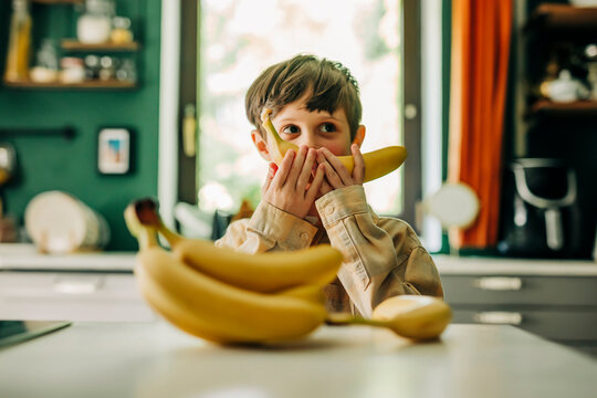Boy playing with bananas in a kitchen promoting healthy eating and fun.