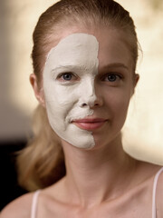 A young woman with Caucasian descent, wearing a half-face mask, indulges in a calming skincare...