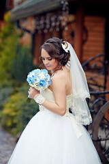 A bride is holding a bouquet of flowers and wearing a white dress. The flowers are blue and white,...