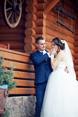 A bride and groom are standing outside of a log cabin. The bride is wiping her nose with her hand