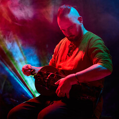 A musician skillfully plays the hurdy-gurdy beneath vibrant red and blue stage lights. Concept of...