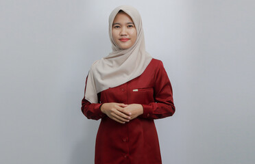 A confident Muslim woman wearing a beige hijab and red shirt poses with her arms crossed against a...