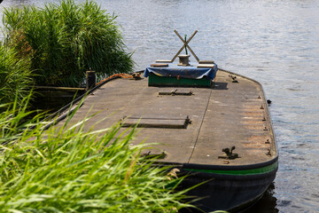 Old Flat-Bottomed Boat Moored on River with Tall Grass in Foreground