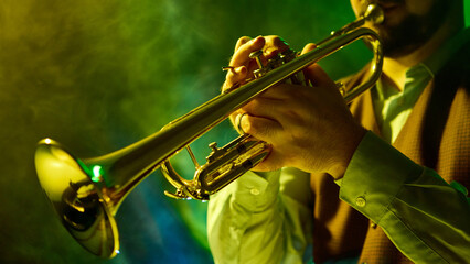 A musician plays the trumpet amid vibrant green and yellow stage lighting, creating a mesmerizing...