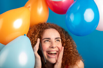 Redhead woman receiving good news on phone surrounded by balloons