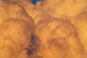 Massive orange thunderclouds illuminated by the evening sun with a deep blue sky peeking through. A dramatic natural scene capturing the power and beauty of the atmosphere.