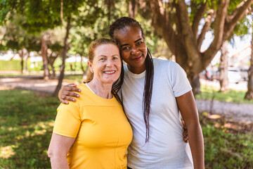 Obraz premium Two women, one senior and the other middle-aged, are hugging, demonstrating genuine interracial friendship and care in a park setting