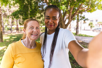 Two happy women, one senior and one middle age, are taking a selfie in a park, celebrating their friendship
