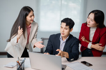 Three asian businesspeople are discussing a project while looking at a laptop, analyzing data and planning their next business strategy inside a modern office