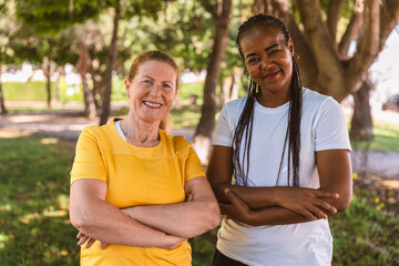 Senior and young women smiling with crossed arms, enjoying time together in a park, representing...