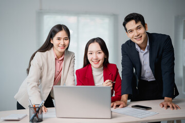 Fototapeta premium Three asian businesspeople are smiling and working together using laptop in modern office, discussing and sharing ideas for their next project