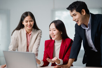 Three asian businesspeople are collaborating on a project, looking at a laptop and discussing ideas in a modern office setting, showcasing teamwork and collaboration