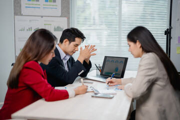 Marketing team analyzing financial reports displayed on laptop and taking notes during strategy planning meeting in modern office, facing challenges and seeking solutions