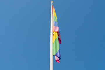 Rainbow flag on a flagpole in the wind against a blue sky