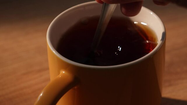 Hand drops sugar cube into cup of black tea and stirring