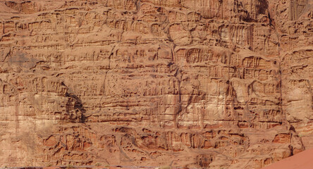 Orange rock wall with cracks and holes on arid terrain in Wadi Rum, Jordan