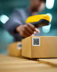 A person scans a QR code on a cardboard package using a yellow handheld barcode scanner.