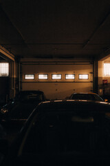 Dimly lit indoor parking garage with several parked cars, atmospheric warm lighting through small...