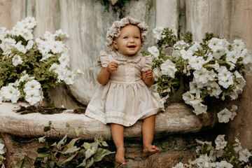 happy little girl in vintage clothes sitting near flower bed in village in summer