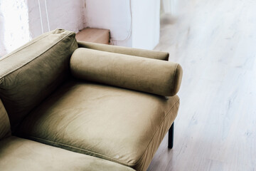 Modern olive green sofa with a unique cylindrical armrest displayed in bright interior space
