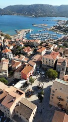 Vue sur la place de la R&eacute;publique &agrave; Porto-Vecchio, entour&eacute;e de maisons en pierre et de b&acirc;timents color&eacute;s, avec les tables d&rsquo;un restaurant install&eacute;es en terrasse. En arri&egrave;re-plan, le port de plaisance 