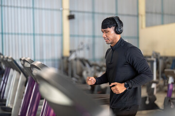 Fitness and Wellness. Man jogging on treadmill in gym with headphones.