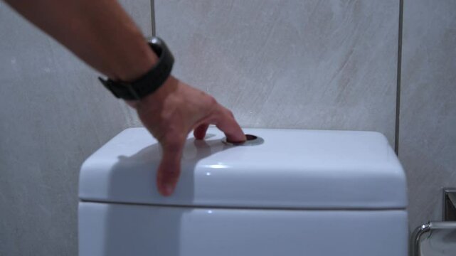 Close-up of hand pressing flush button on modern toilet. Great for hygiene, sanitation, or bathroom product use.