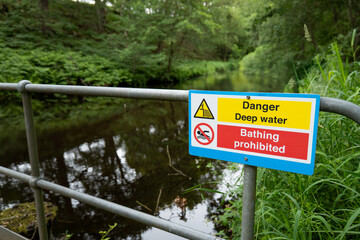 Safety sign warns of deep water and prohibits bathing and wild swimming at a quiet reservoir in...