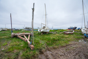 Abandoned Boats – Coastal Landscape. A collection of weathered sailboats rests on a muddy tidal...