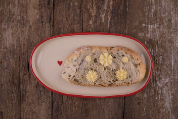 Butter in the form of flowers on a piece of bread on a plate on a wooden table.