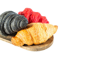 Red, black and classic croissants on a wooden board. Isolated on white.