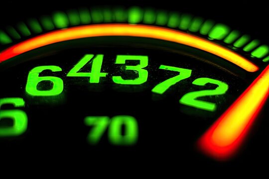 Close-up of a glowing, vintage-style speedometer.  Bright green numbers on a black dial, with orange/red highlights.  Focus on the numbers - Powered by Adobe