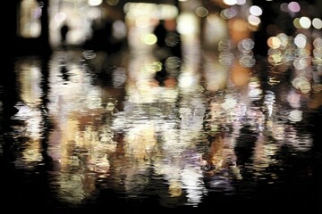 Abstract reflections of a bustling night market.  Blurred figures and lights reflected in rippled water