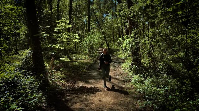 Frightened woman running away from serial killer in forest. Terrified female escaping from maniac through wooded trail. Scared lady fleeing from murderer along shadowy forest path