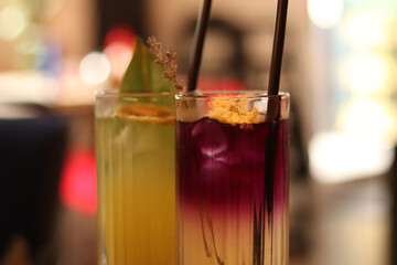 Delicious lemonades in glass cups. Refreshing drinks in a cafe or restaurant. Lavender and citrus lemonade close-up. Glass cups with delicious bright drinks. Cocktails with straws. Drinks with ice