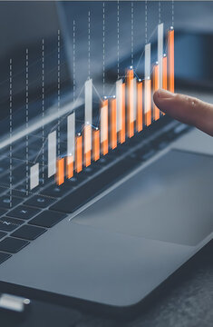 Financial Growth Visualization: A finger interacting with a transparent financial graph overlaid on a laptop, symbolizing growth, trends, and analysis in the realm of business and finance.