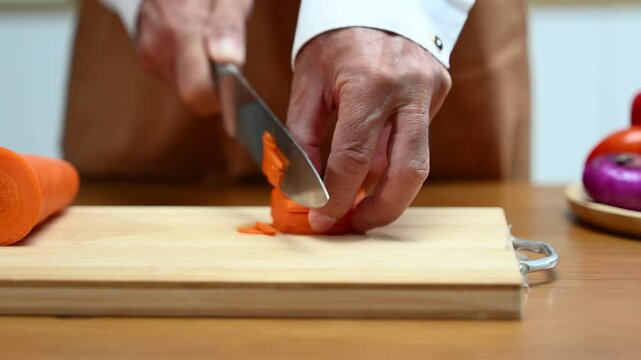 Closeup of hands slicing fresh carrot on a wooden board in clean kitchen. Healthy cooking, diet food prep, organic vegetables,
