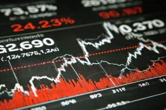 Close-up of a financial data display showing fluctuating stock market graphs and percentages.  Red and white lines depict trends.  Large numeric values are present