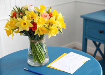 Fresh daffodils in a beautiful bouquet sitting on a blue table with a greeting card nearby