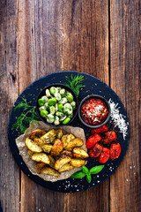 Boiled broad bean with roasted potatoes and cherry tomatoes with tomato pesto on wooden table